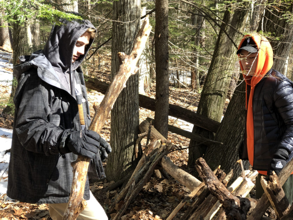 Students learn to build debris shelters in the woods near campus.