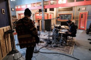 Students recording bass, drums, and vocals in the studio.